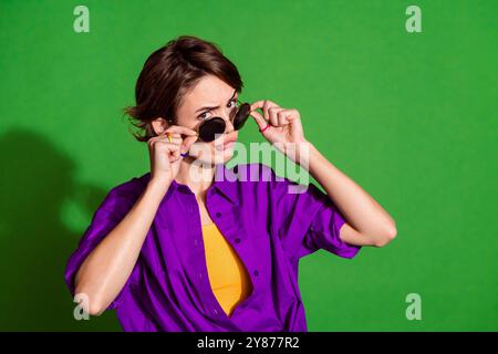 Foto ritratto di una giovane donna positiva con i capelli di Bob che indossano un elegante occhiale da sole, che sembra sospetta isolata su sfondo di colore verde Foto Stock