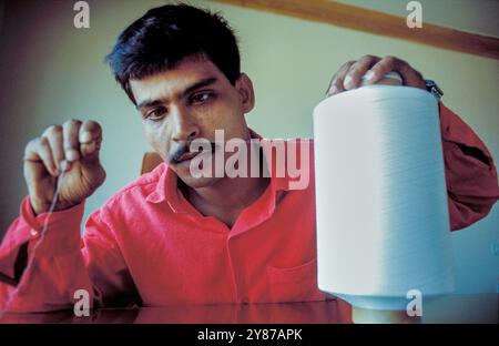 Bangladesh, Dacca, un lavoratore mostra un filo su una bobina in una fabbrica tessile. Foto Stock