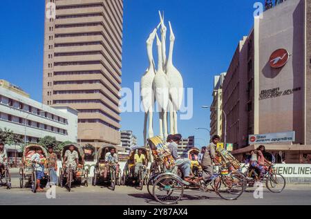 Bangladesh, Dacca, autisti di risciò in attesa dei clienti di fronte a una scultura nel quartiere degli uffici. Foto Stock