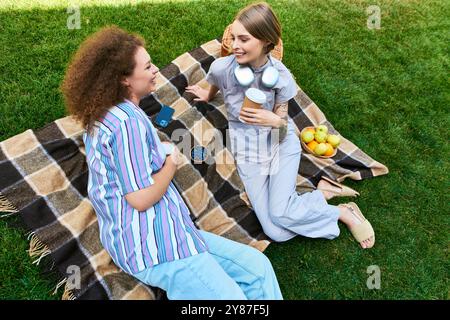 Due amici si rilassano insieme su una coperta accogliente, ridendo e gustando spuntini al sole. Foto Stock