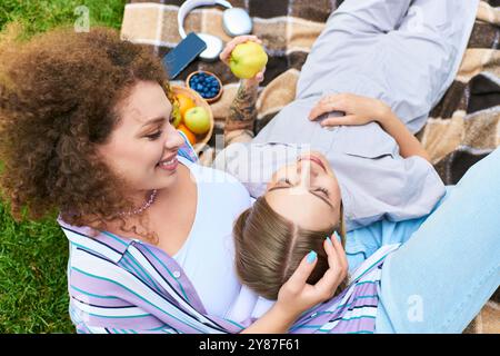 Due amici si rilassano su una coperta, condividendo i momenti migliori con frutta e sorrisi sotto il sole. Foto Stock
