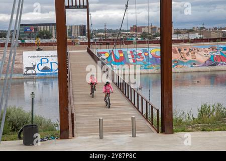 Pueblo, Colorado - i ciclisti attraversano un ponte sul fiume Arkansas, dove i murales e una pista ciclabile costeggiano l'argine. L'argine è stato costruito dopo una disa Foto Stock