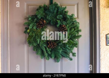 Questa corona, fatta di freschi rami sempreverdi e decorata con coni di pino, è appesa su una porta d'ingresso Foto Stock