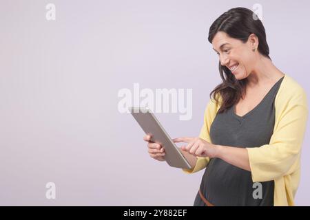 La donna sorride mentre lavora con il suo tablet. Isolato su sfondo viola. Foto Stock