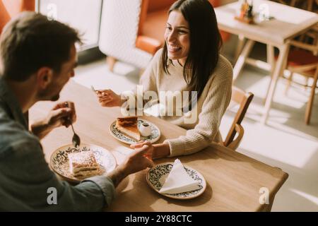 In un caffè caldo e invitante, una coppia condivide risate e deliziose prelibatezze, assaporando caffè e pasticcini mentre si crogiola al sole del pomeriggio. Foto Stock