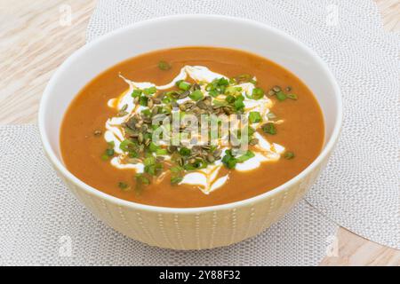 ciotola di zuppa a base di zucca, patate dolci e carote, con semi di zucca, acido, panna e cipolla verde sul tavolo pronta per essere mangiata Foto Stock