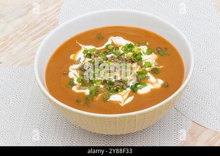 ciotola di zuppa a base di zucca, patate dolci e carote, con semi di zucca, acido, panna e cipolla verde sul tavolo pronta per essere mangiata Foto Stock