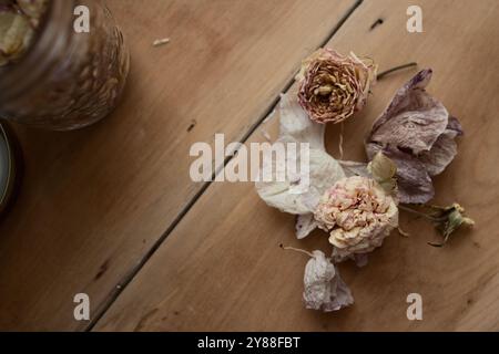 In questa scena autunnale, i fiori secchi riposano su uno sfondo rustico in legno per essere conservati in vasetti mason. I vasetti conserveranno i petali di rosa essiccati. Foto Stock