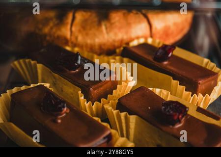 Una vetrina con una varietà di torte e cupcake. Dessert al cioccolato con ciliegia in cima. Le torte sono disposte in fila, con alcune di esse Foto Stock