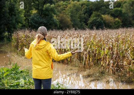 Un lavoratore agricolo preoccupato che guardava il campo di mais allagato dopo la pioggia. Impatto di condizioni meteorologiche estreme e inondazioni sull'agricoltura Foto Stock