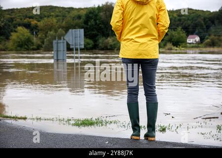 Inondazione dopo una pioggia intensa. Donna preoccupata che guarda il fiume allagato. Condizioni meteorologiche estreme e calamità naturali Foto Stock