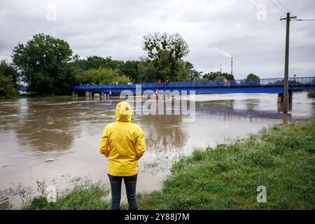 Inondazione dopo una pioggia intensa. Donna preoccupata con l'impermeabile che guarda il fiume allagato. Condizioni meteorologiche estreme e calamità naturali Foto Stock