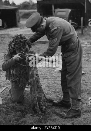 Le guardie domestiche insegnarono l'arte del mimetismo -- Un sergente delle guardie istruisce una Guardia interna. Parte dell'allenamento per le guardie domestiche nel campo è l'arte del mimetismo. In un campo nel sud dell'Inghilterra, alle guardie domestiche fu data una lezione e una dimostrazione pratica che mostravano come si potevano nascondere sia nelle città che nel paese. L'ufficiale mimetico ha illustrato con l'aiuto di rifiuti provenienti dai bidoni della spazzatura, come fosse possibile per un uomo nascondersi a Londra se fosse necessario combattere per strada. 22 febbraio 1943. (Foto di London News Agency Photos). Foto Stock