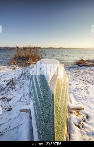 Barca rovesciata nella neve sul lungolago all'alba, Niederzell, Reichenau, lago di Costanza, Baden-Wuerttemberg, Germania, Europa Foto Stock