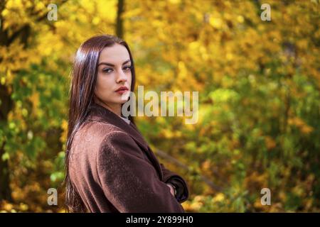 Giovane bella donna in mantello marrone nel parco in autunno Foto Stock