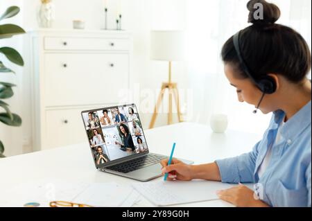 Webinar. Conferenza finanziaria online. Vista laterale della donna caucasica che incontra online persone multirazziali e tutor, ascolta lezioni, migliora le sue conoscenze, prende appunti, brainstorming di gruppo Foto Stock
