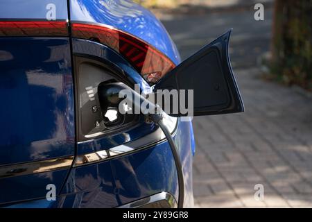 Un'auto elettrica blu che si ricarica su un caricabatterie domestico in una giornata di sole Foto Stock