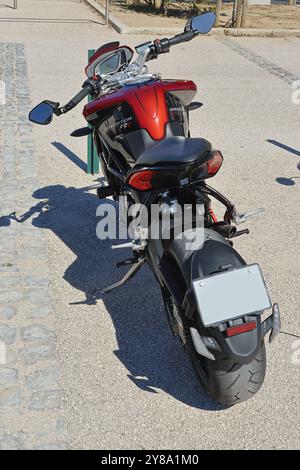 Motocicletta rossa e nera parcheggiata sul lato di una strada con la sua ombra gettata sul marciapiede Foto Stock