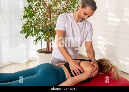 Osteopata maschile che esegue un massaggio miofasciale sulla spalla di una donna sdraiata su un lettino massaggiante Foto Stock