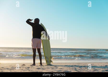 Uomo afroamericano anziano con viste di surf al mare e al cielo dalla spiaggia Foto Stock