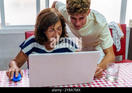 Adolescente che insegna alla nonna di 70 anni a utilizzare un notebook, colmando il divario digitale Foto Stock