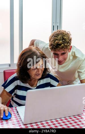 Adolescente che insegna alla nonna di 70 anni a utilizzare un notebook, colmando il divario digitale Foto Stock