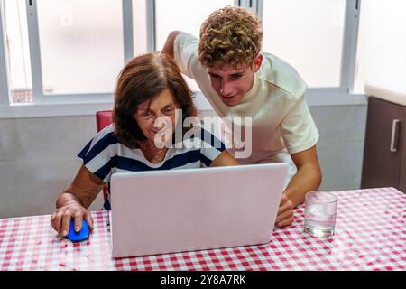 Adolescente che insegna alla nonna di 70 anni a utilizzare un notebook, colmando il divario digitale Foto Stock