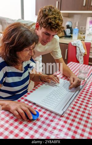Adolescente che insegna alla nonna di 70 anni a utilizzare un notebook, colmando il divario digitale Foto Stock