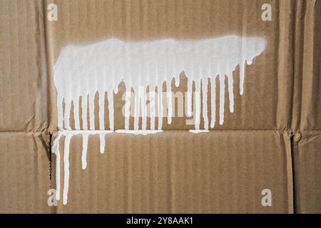 Una striscia di vernice spray bianca con gocciolamenti su un cartone Foto Stock