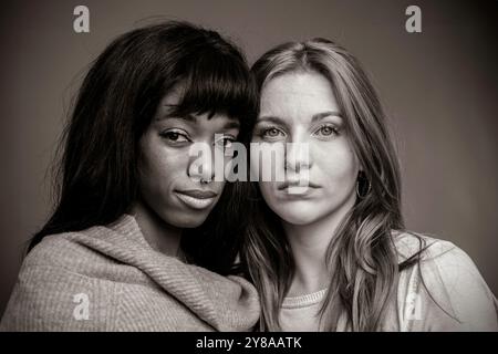 Due giovani donne di diverse etnie condividono un momento intenso e serio in un ritratto dai toni seppia. L'immagine cattura una profonda emozione Foto Stock