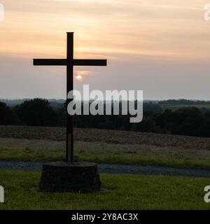 Una tranquilla foresta al tramonto, caratterizzata da una semplice croce di legno in una piccola radura tra alberi alti Foto Stock
