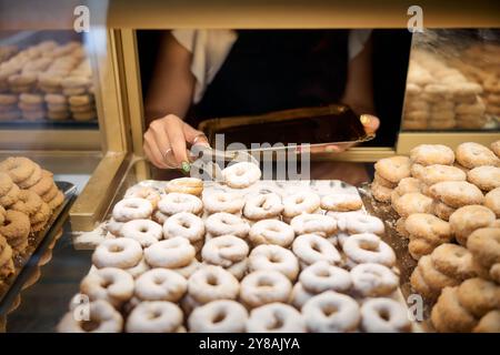 Un fornaio usa le pinze per prendere una pasticceria a base di zucchero a velo Foto Stock