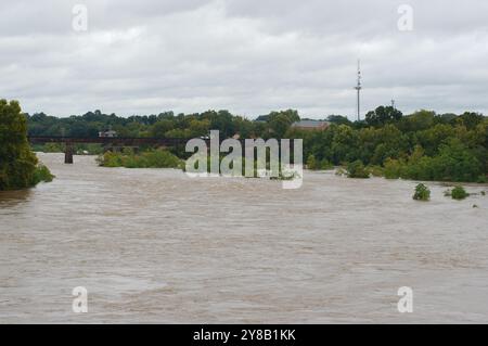 Ampia visuale dall'alto verso il basso per un rapido movimento, slancinante e fangoso flusso d'acqua di fiume marrone argilla che rotola con tappi bianchi. Alberi verdi dal ponte Foto Stock