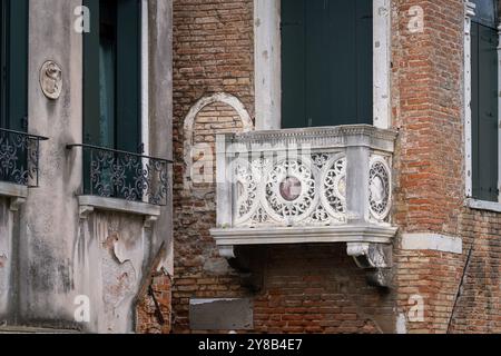 Facciata con finestre e balcone in pietra intagliata a Venezia. Balkony in pietra scolpita di un vecchio edificio veneziano. Foto Stock
