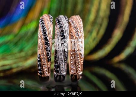 un set di tre anelli. gioielli sullo sfondo delle piume di pavone. tre anelli con pietre. fedi nuziali in oro e argento. Foto Stock