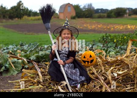 Bambina in costume da strega che gioca nel parco autunnale. Bambino che si diverte a Halloween trucco o trattare. Trucchi o trattamenti per i bambini. Bambino piccolo con jack-o-lan Foto Stock