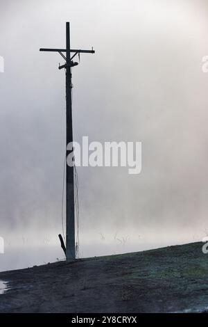 Un polo di energia sembra una croce sopra di esso in piedi in un campo. Il cielo è nuvoloso e il tempo è coperto Foto Stock