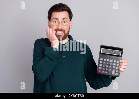 Foto dell'uomo depresso e stressato indossa abiti eleganti calcolatrice da banco da lavoro isolata su sfondo grigio Foto Stock