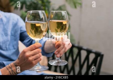 Brindisi di coppia irriconoscibili e bere vino bianco all'aperto in una fattoria in un giardino da vicino Foto Stock