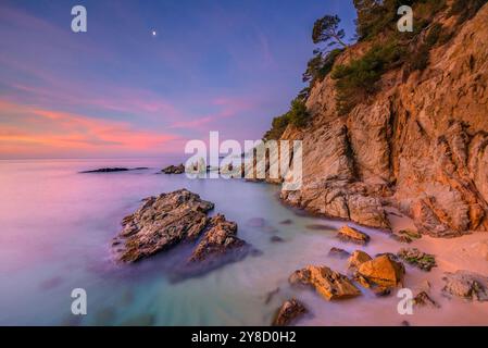 Alba rossa a Cala sa Boadella e con la Luna che scende, a Lloret de Mar, Costa Brava (la Selva, Girona, Catalogna, Spagna) Foto Stock