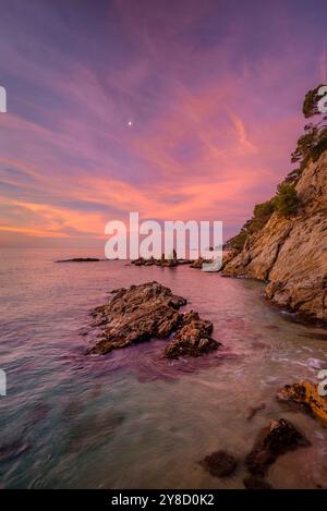 Alba rossa a Cala sa Boadella e con la Luna che scende, a Lloret de Mar, Costa Brava (la Selva, Girona, Catalogna, Spagna) Foto Stock