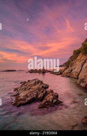 Alba rossa a Cala sa Boadella e con la Luna che scende, a Lloret de Mar, Costa Brava (la Selva, Girona, Catalogna, Spagna) Foto Stock