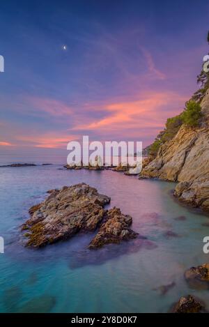 Alba rossa a Cala sa Boadella e con la Luna che scende, a Lloret de Mar, Costa Brava (la Selva, Girona, Catalogna, Spagna) Foto Stock