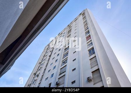 Vista dal basso di un grande edificio in cemento con molte finestre e linee verticali che ne rafforzano la lunghezza. Cielo azzurro come sfondo Foto Stock