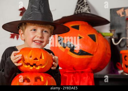 Il ragazzo in costume di Halloween è dietro una pila di zucche intagliate Foto Stock