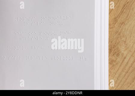 Pagine Braille di un libro. Vista ravvicinata del testo in Braille su carta, posto su una superficie di legno. Temi di accessibilità e concetti educativi. Foto Stock