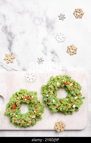 Due corone di cibo verde sono su un tagliere bianco. Le corone sono decorate con spruzzi bianchi e rossi Foto Stock