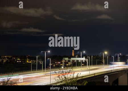 Lunga esposizione notturna di un'autostrada con sentieri leggeri che passano dalle auto, lo skyline della città sullo sfondo e i lampioni che illuminano la scena. Foto Stock