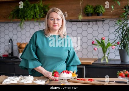 In cucina, la donna prepara un dessert pavlova fatto in casa con fragole fresche, panna montata, mostrando arte culinaria e concetto di preparazione dei dessert Foto Stock