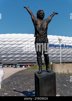 Monaco di Baviera, Germania - 13 agosto 2024. Allianz Arena di Monaco sullo sfondo. Statua del calciatore Gerd Mueller in primo piano, vista esterna. Foto Stock